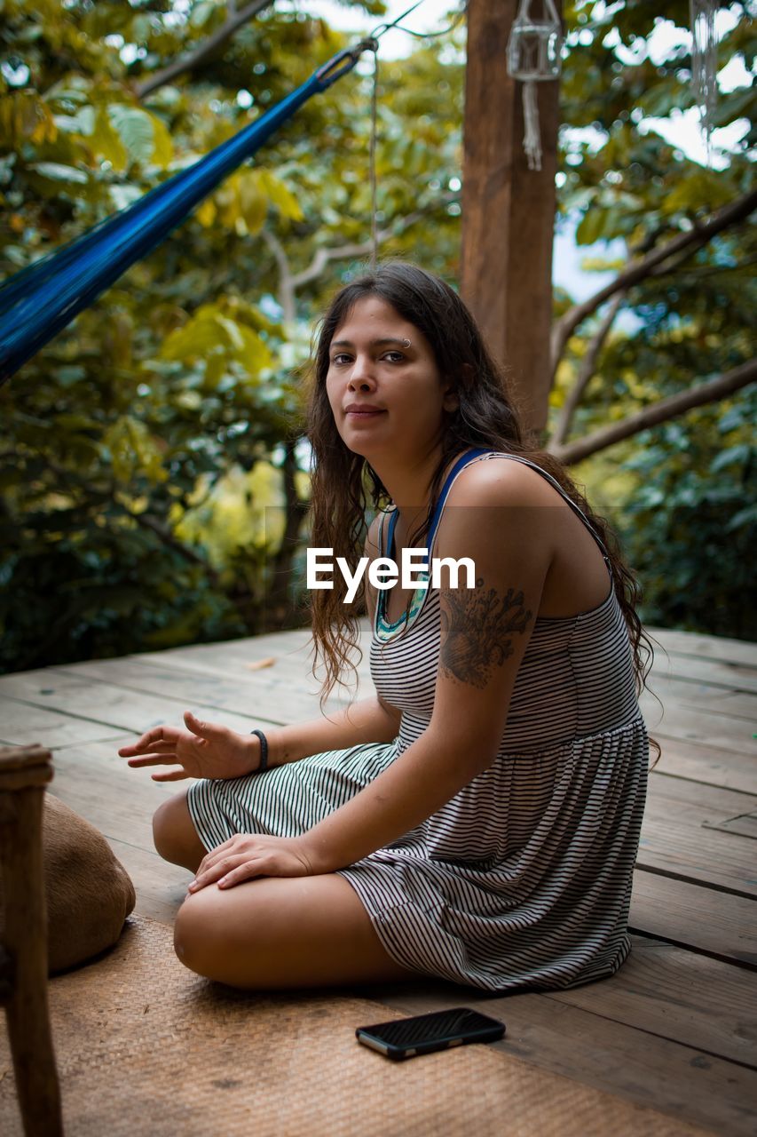 SIDE VIEW OF YOUNG WOMAN SITTING ON TREE