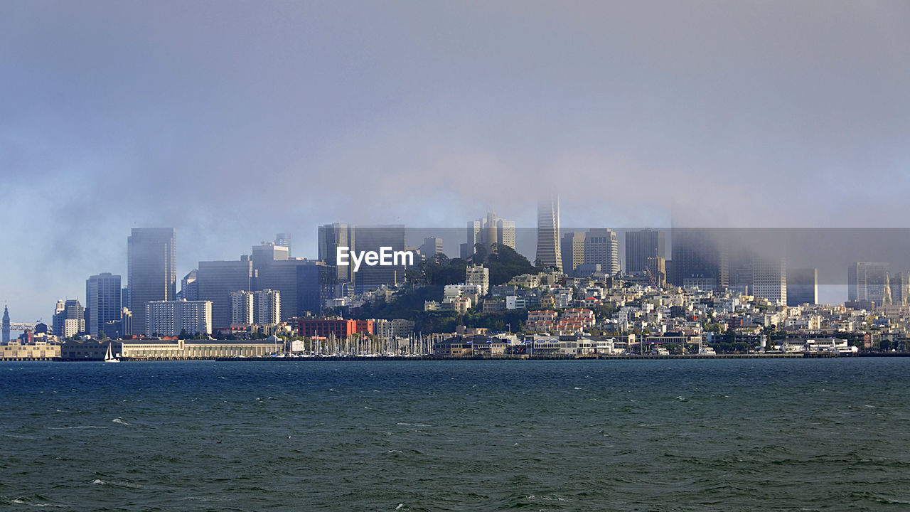 SEA BY MODERN BUILDINGS AGAINST SKY