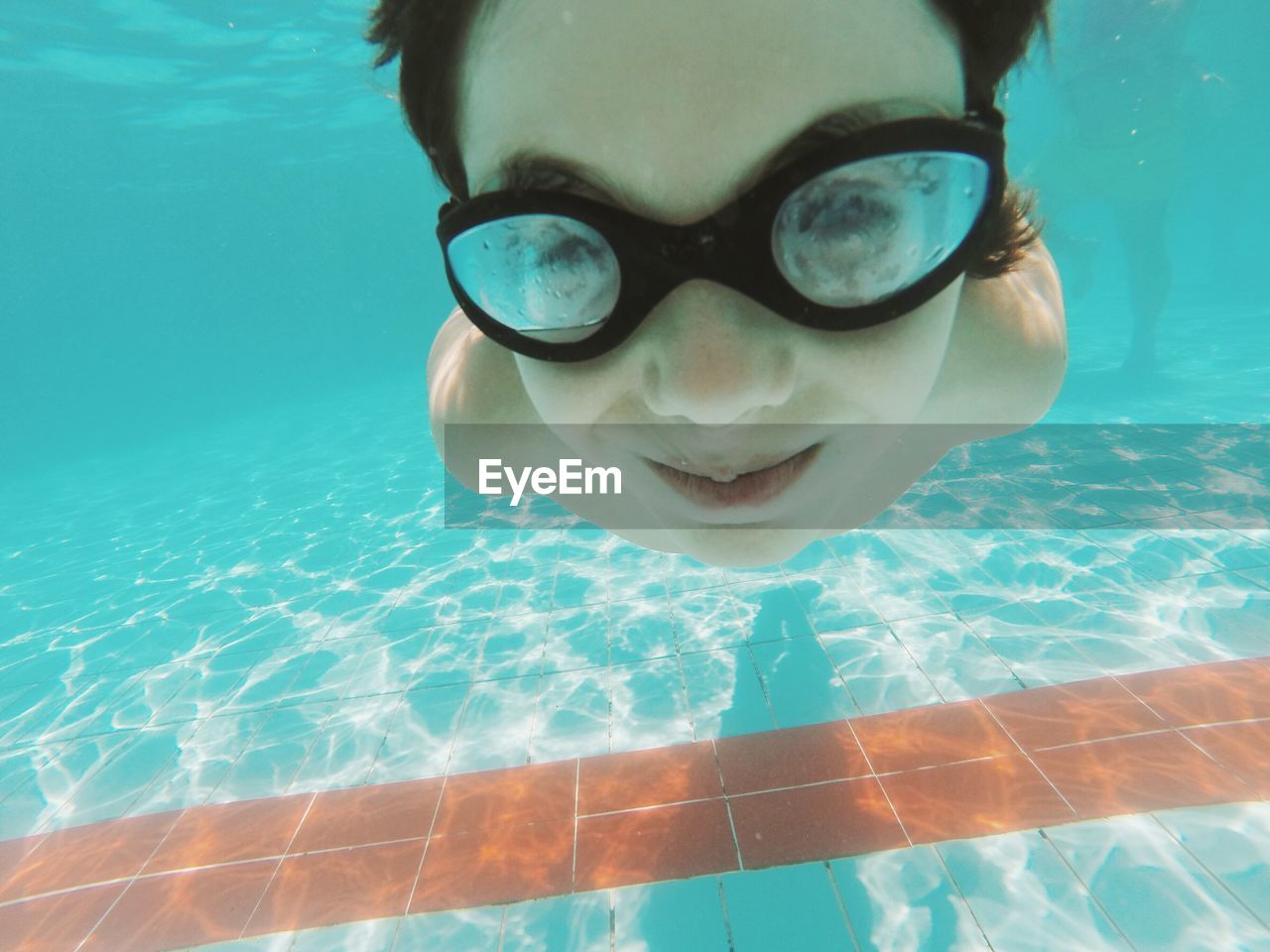 Smiling boy wearing goggles swimming in pool