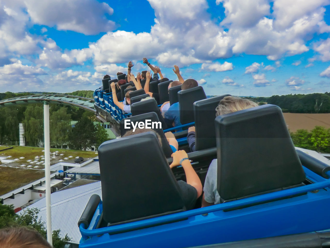 Rear view of people sitting in rollercoaster against cloudy sky