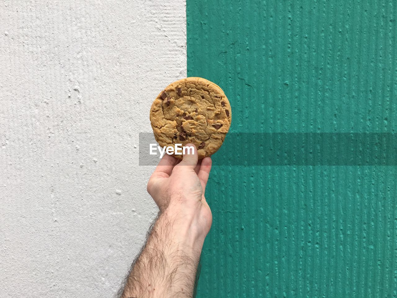 Cropped image of hand holding cookie against wall