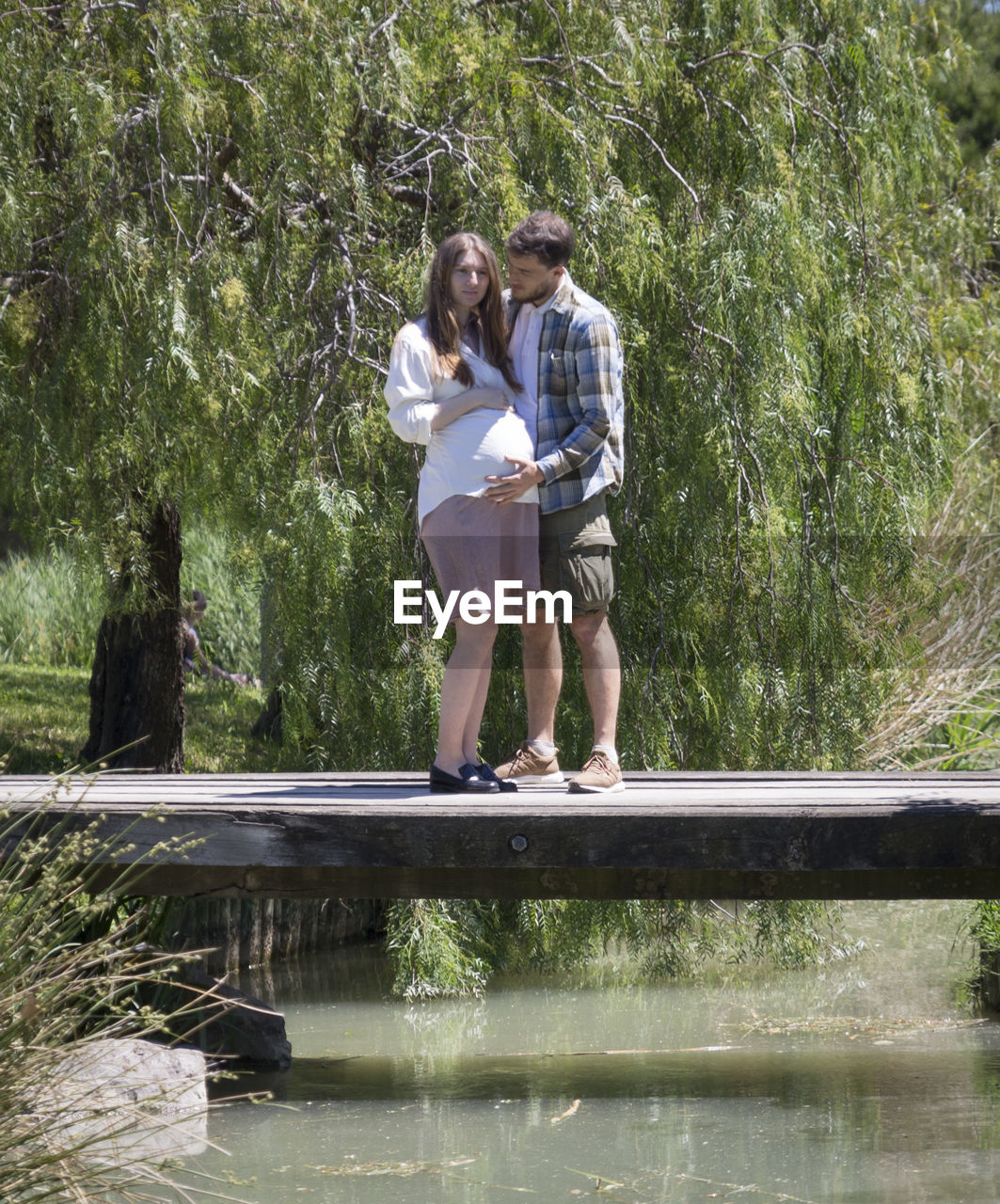 Full length of couple standing on bridge by trees