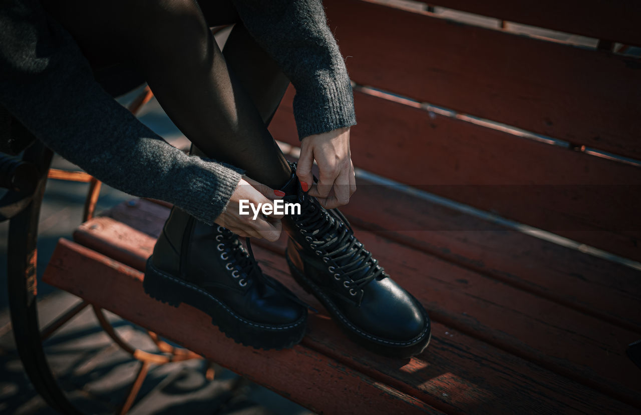 Low section of woman tying shoelace while sitting on bench