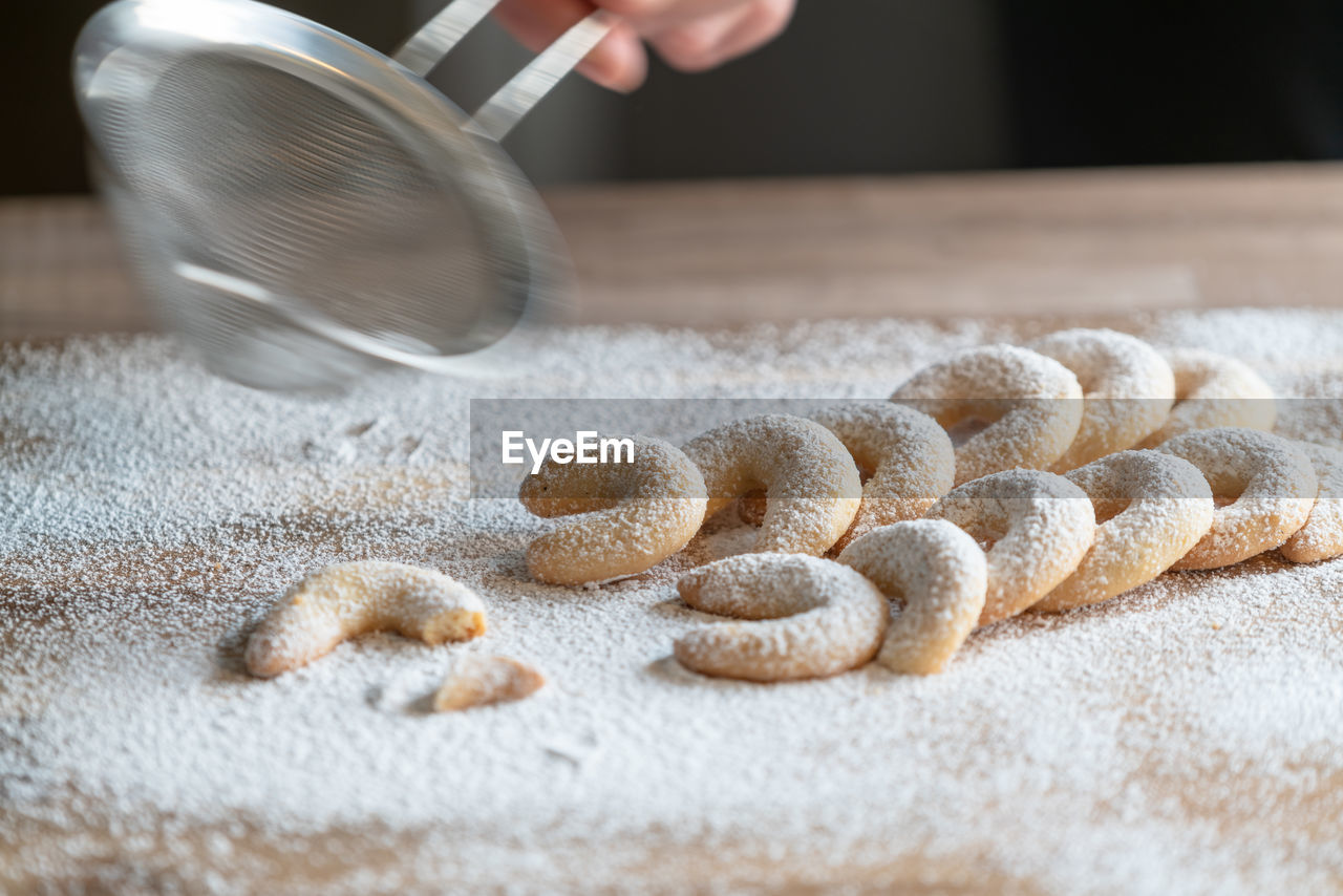 Cropped hand of person sprinkling powdered sugar with strainer on cookies over table 