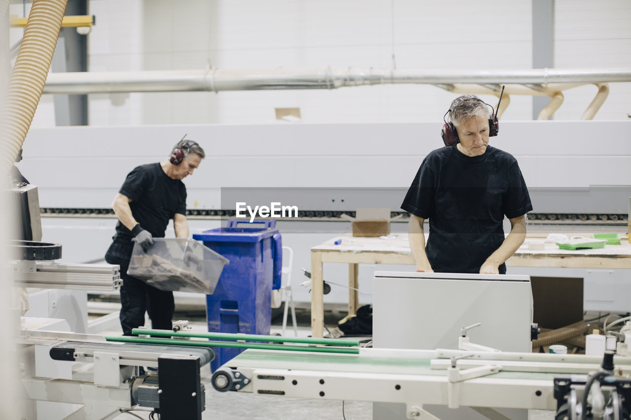 Mature man operating machine in industry while coworker working in background