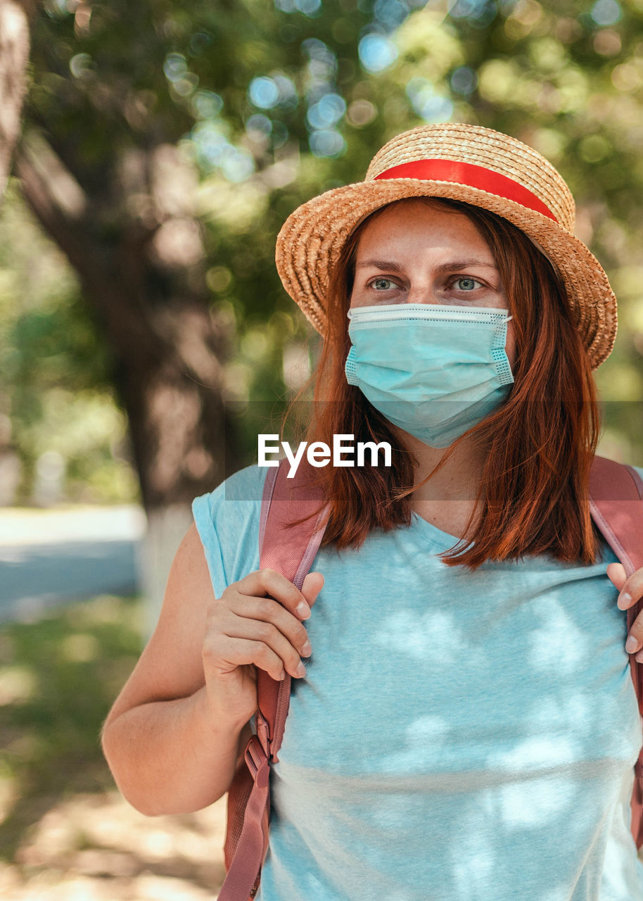 Caucasian tourist girl in summer straw hat with  backpack and  protective mask. travel and vacation