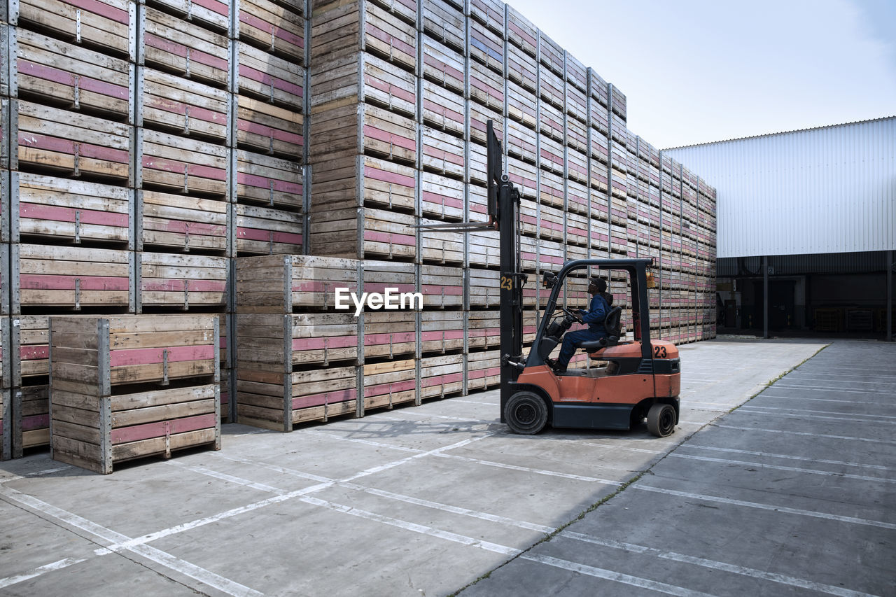 Worker on forklift and stacks of crates on factory yard