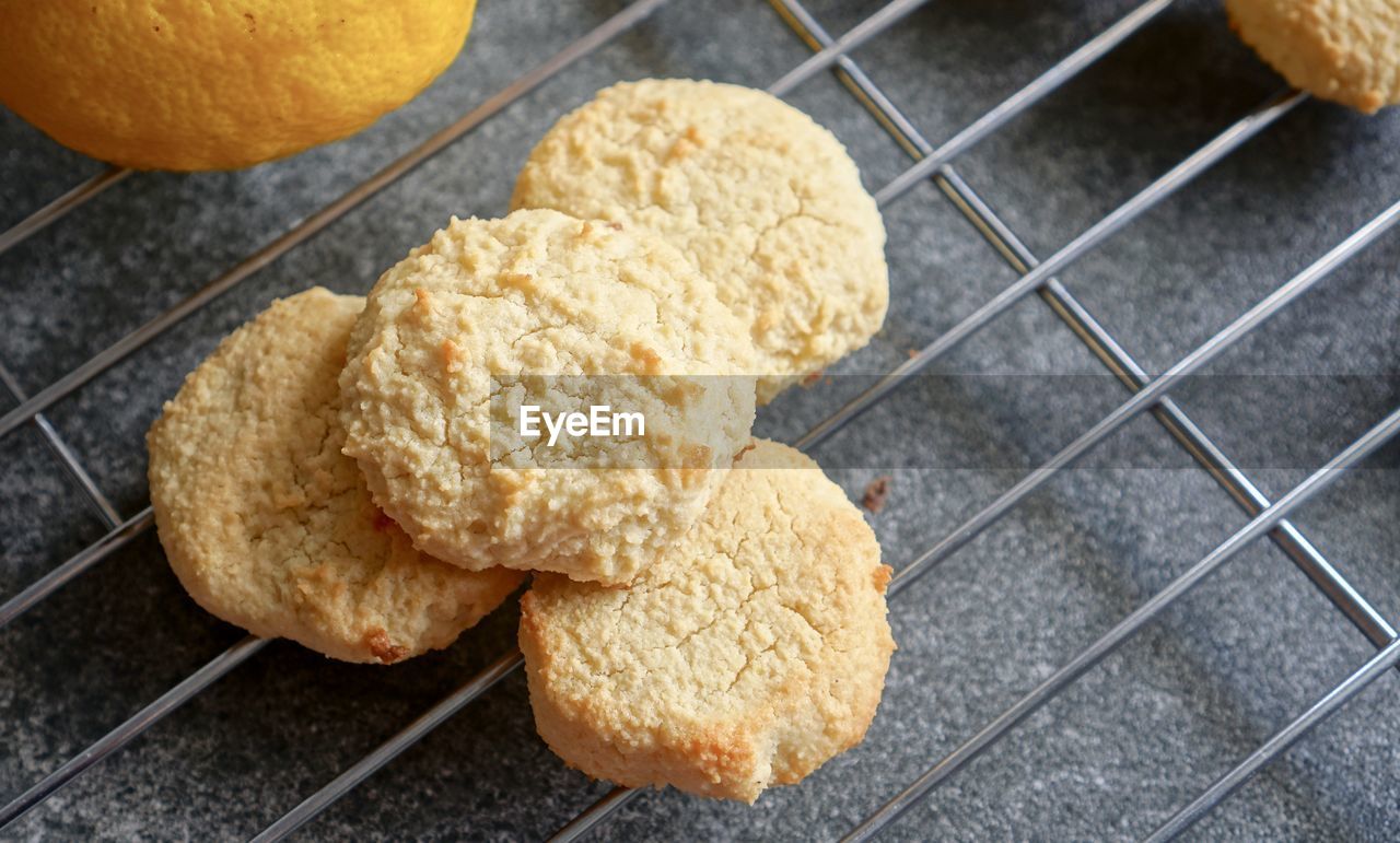 Lemon cookies on cooling, baking rack with part of lemon fruit, on grey background.