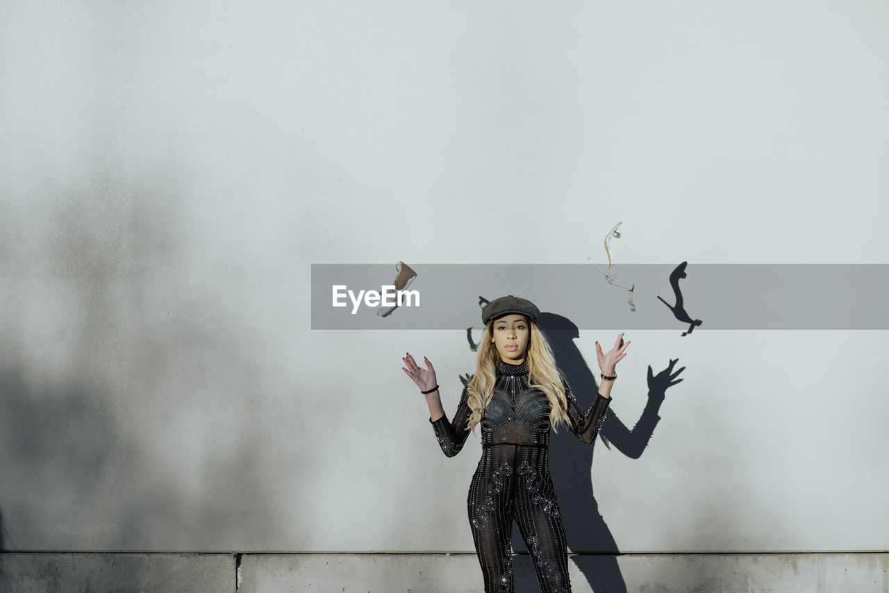 Young black woman throwing her shoes in the air next to a white wall and wearing a hat in the city on a sunny day