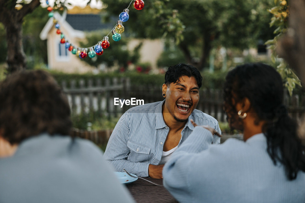 Cheerful young man enjoying while talking to female friend in back yard at dinner party