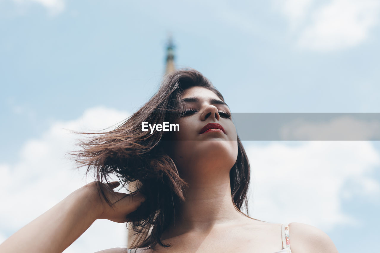 Low angle view of thoughtful young woman against sky