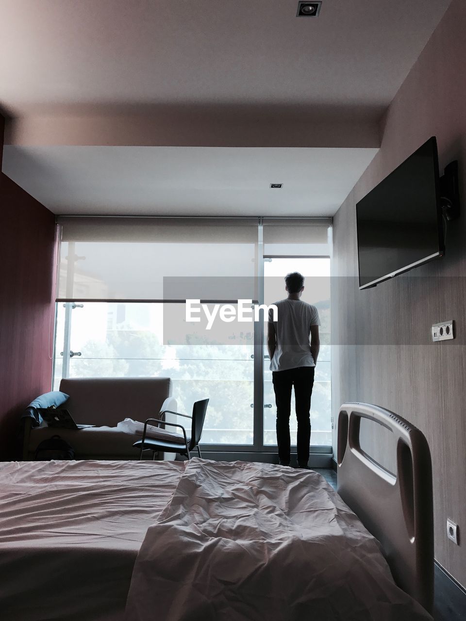 Rear view of man standing by window in hospital ward