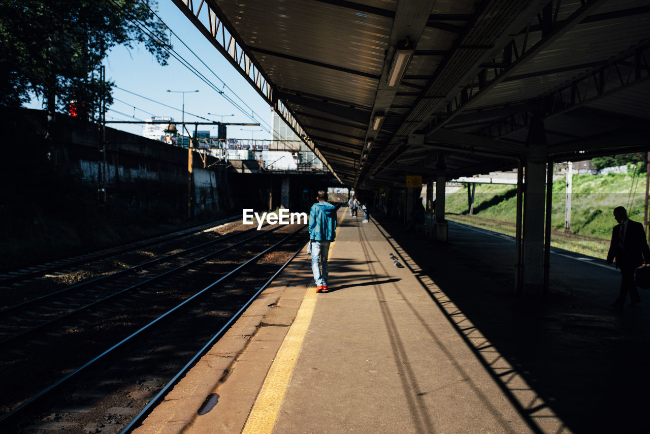 REAR VIEW OF PERSON WALKING ON RAILROAD STATION