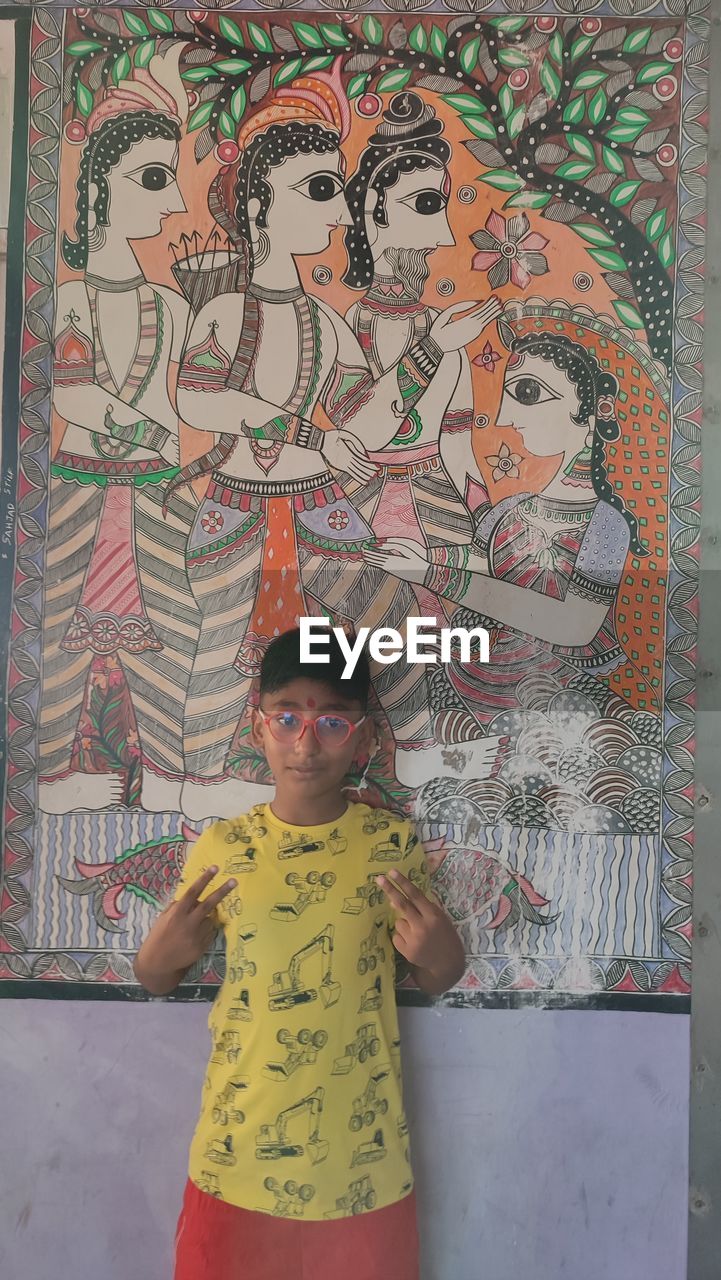 one person, art, front view, standing, creativity, mural, child, portrait, looking at camera, childhood, three quarter length, casual clothing, multi colored, pattern, painting, lifestyles, day, wall - building feature, men, leisure activity, representation, smiling, women, clothing, drawing, indoors, architecture, person