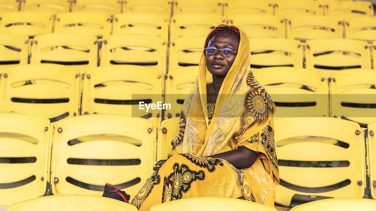 African woman in beautiful yellow suit sitting alone on an empty audience stand in accra ghana,