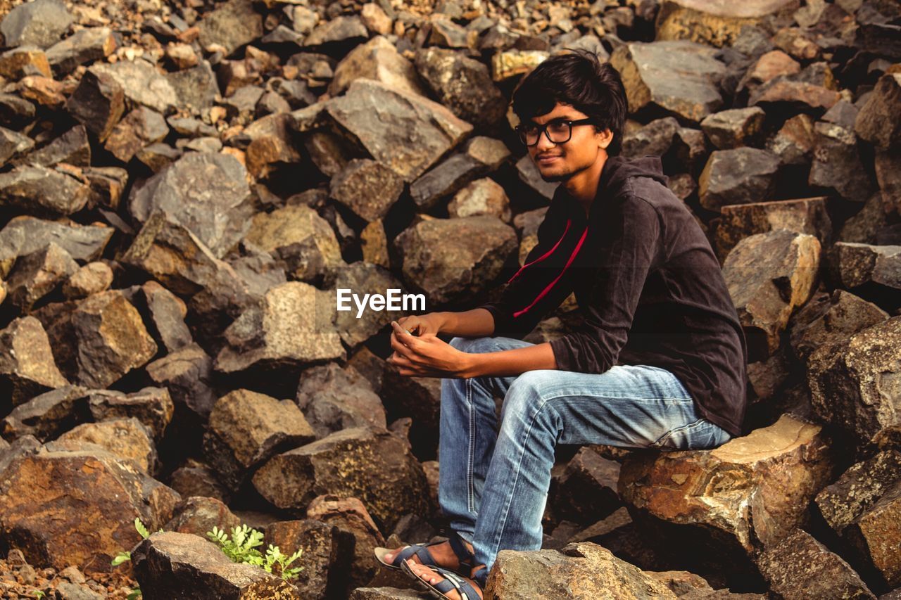 Young man looking away while sitting on rock