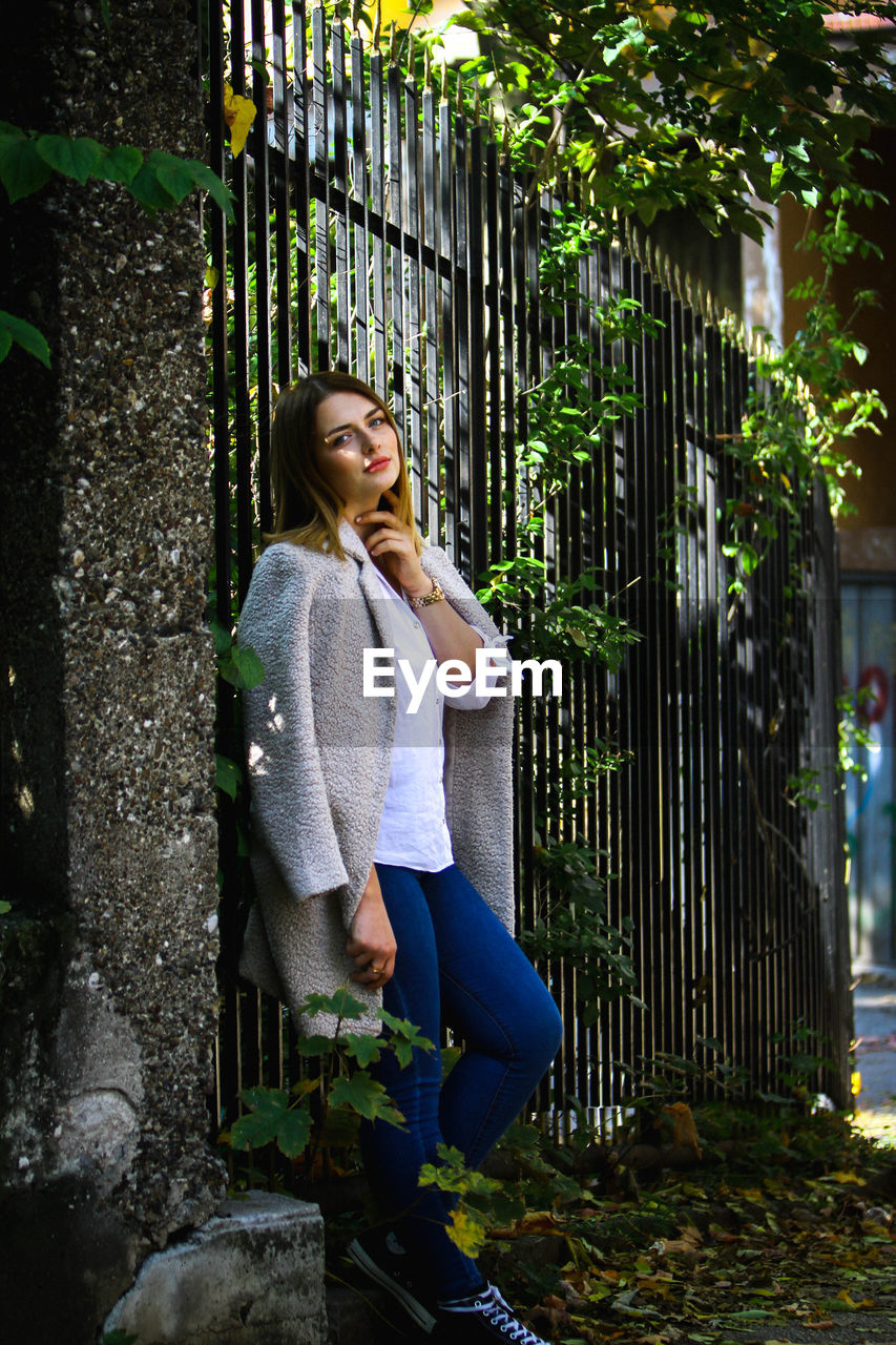 Portrait of young woman standing by fence