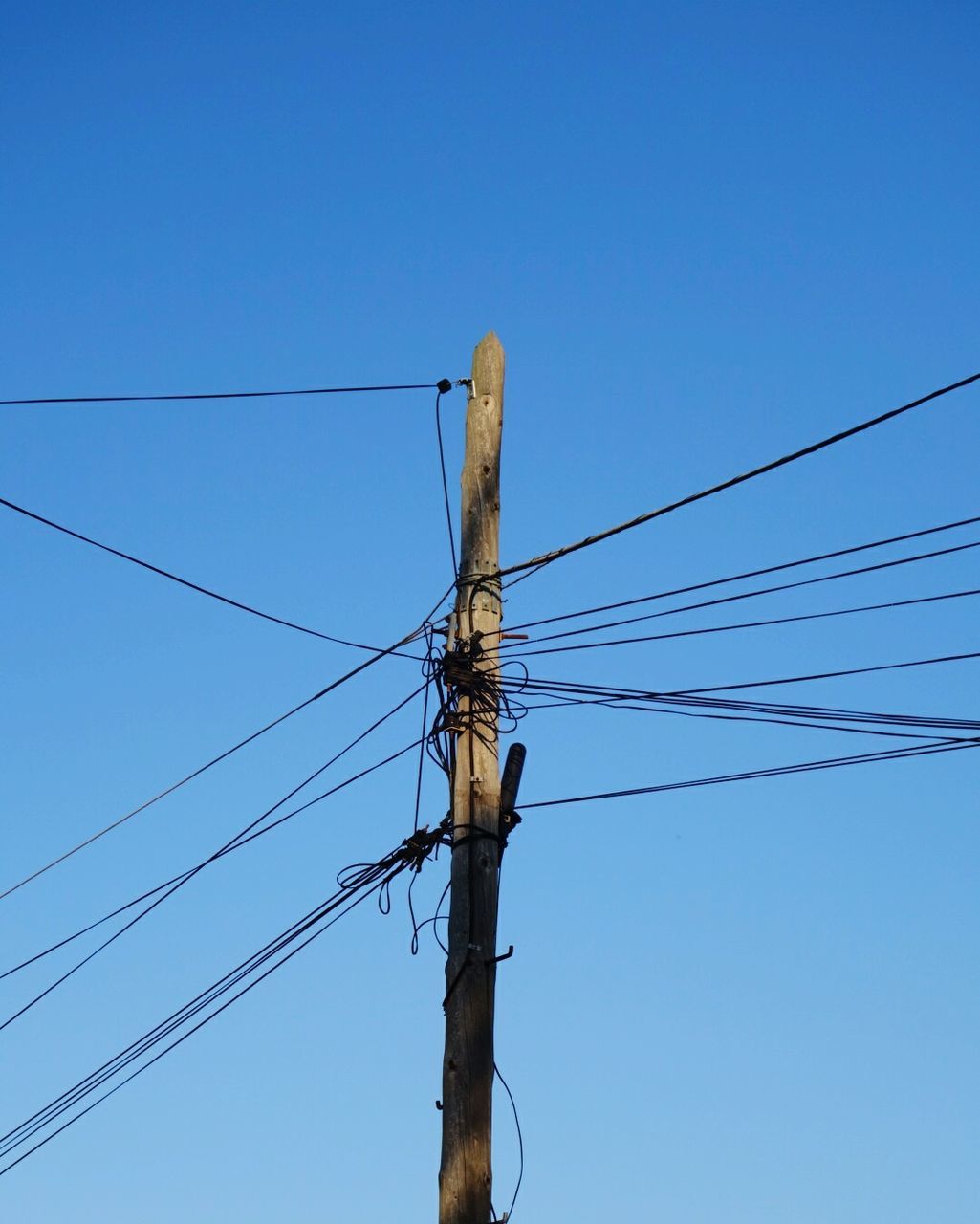 Low angle view of telephone pole against clear blue sky