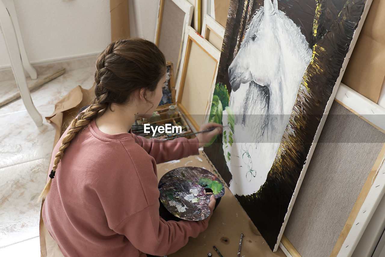 High angle view of teenage girl painting horse on canvas at home