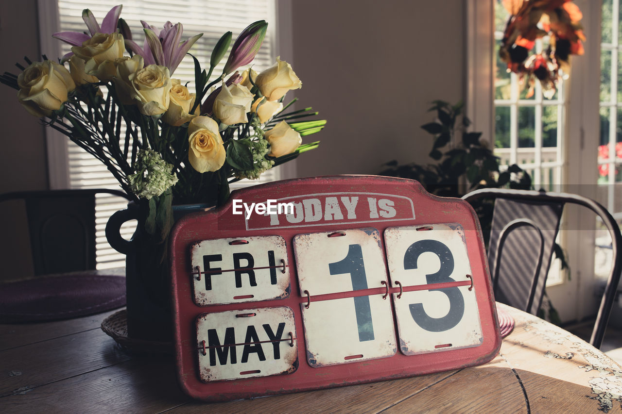 Old-fashioned calendar by flower vase on table