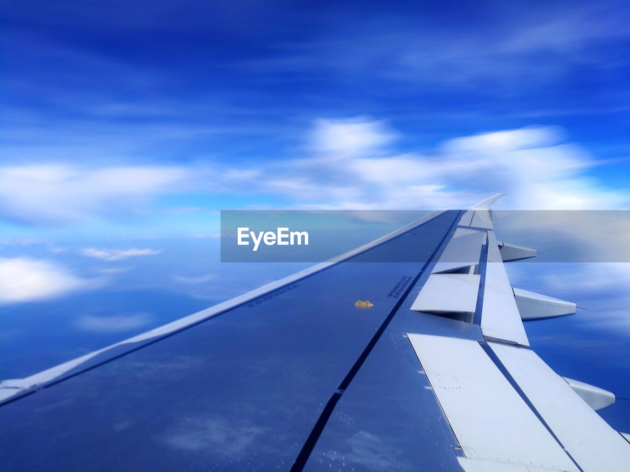 LOW ANGLE VIEW OF AIRPLANE WING AGAINST CLOUDS