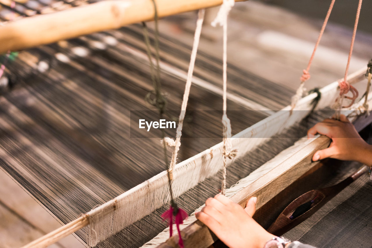 Cropped hands of person holding loom while working in textile industry