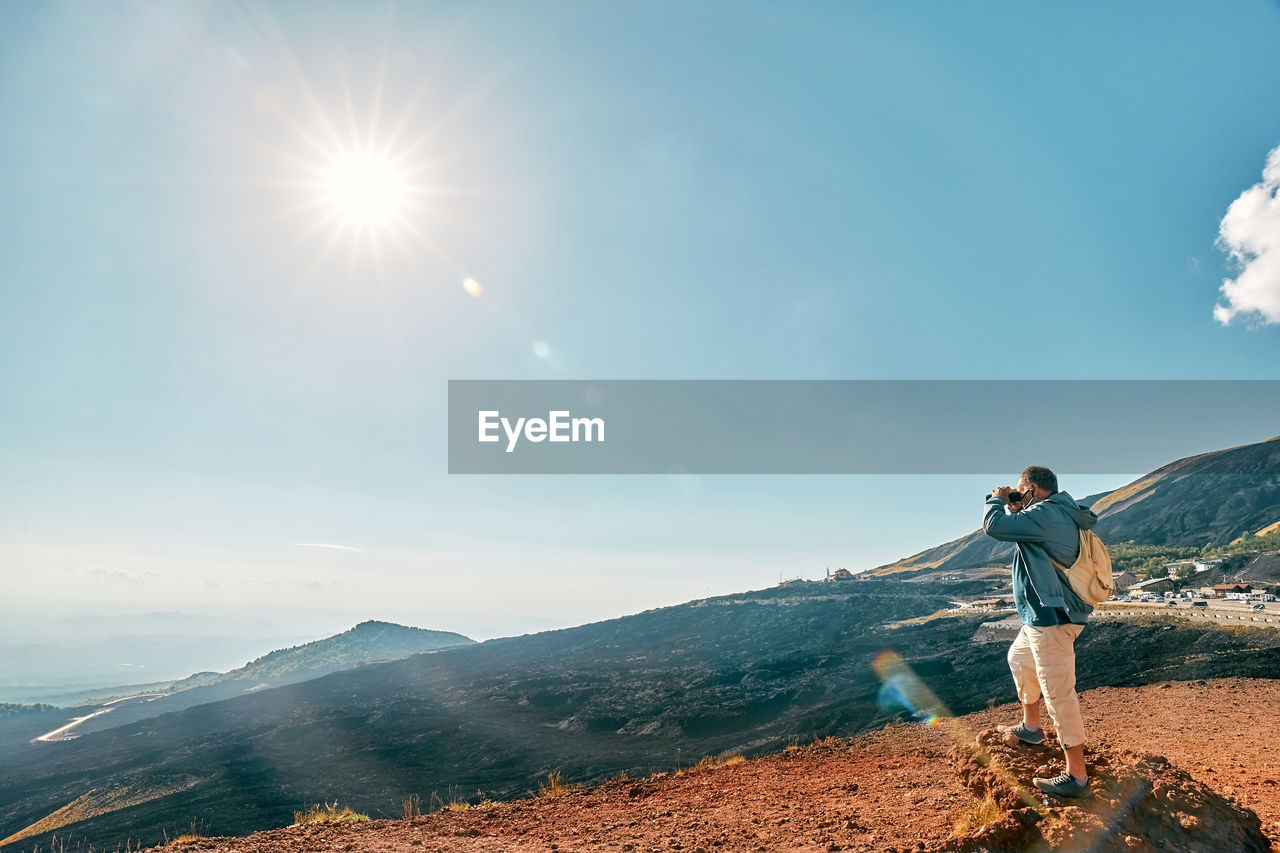 Rear view of man looking through binoculars at panoramic view of colorful summits of  volcano etna