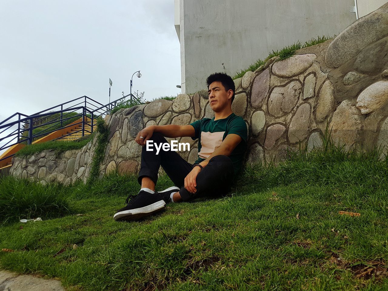 Low angle view of young man sitting on field against wall