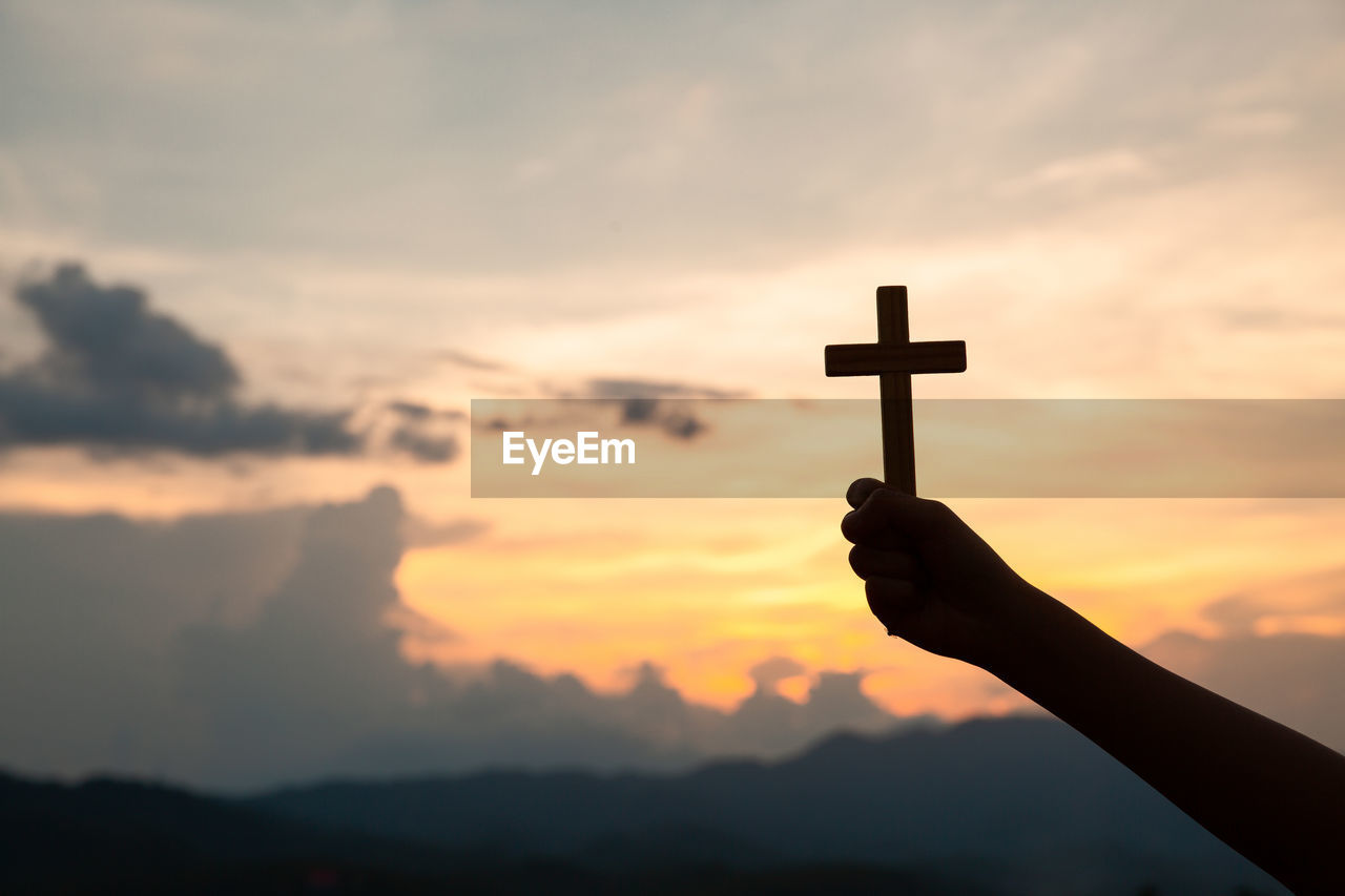 Hands holding wooden cross on sky background, crucifix, symbol of faith.