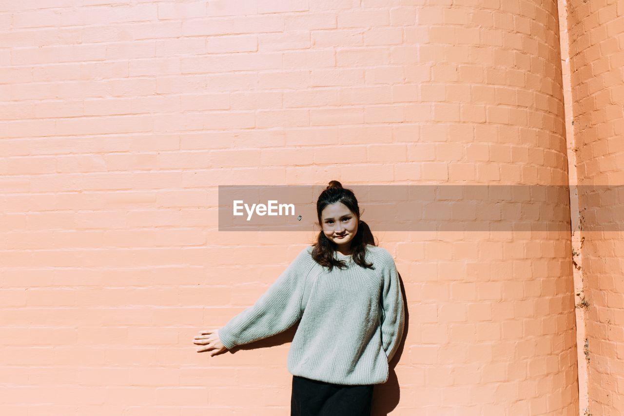 Portrait of smiling young woman standing against wall