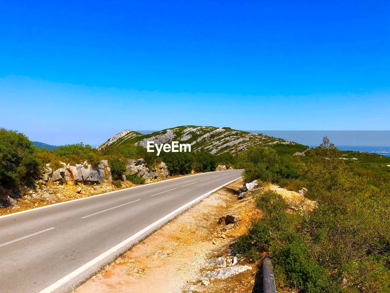 Road leading towards mountain against blue sky