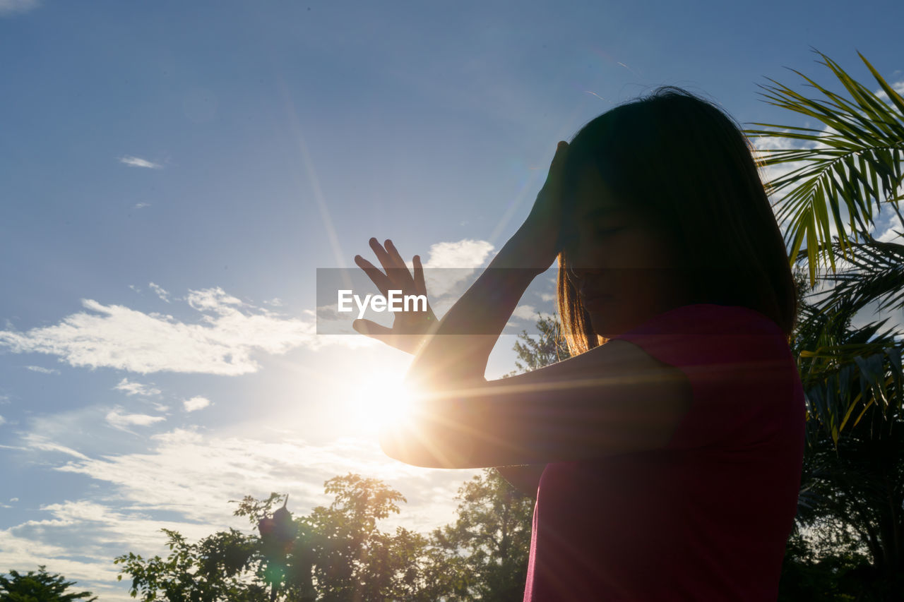 LOW ANGLE VIEW OF WOMAN STANDING AGAINST SUN