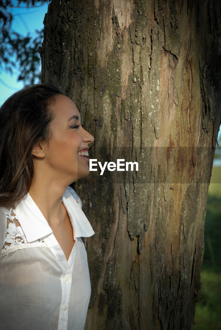 YOUNG WOMAN LOOKING AWAY WHILE TREE TRUNK