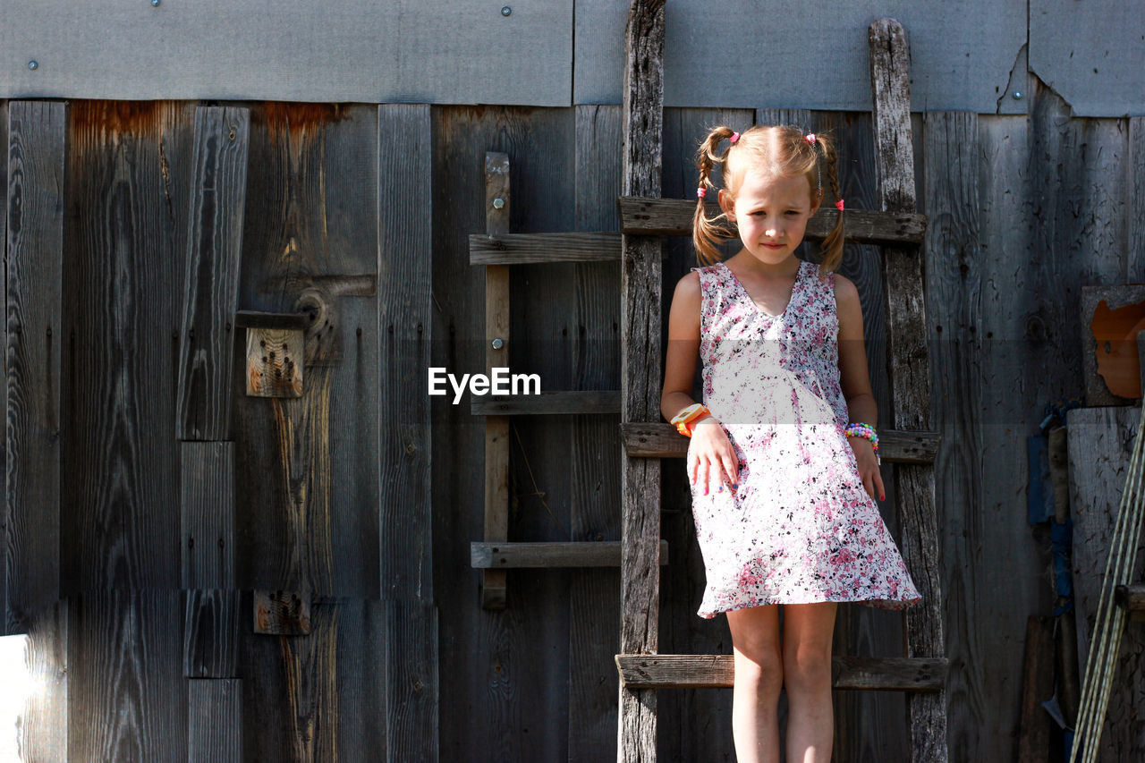 Girl standing on ladder against wooden wall