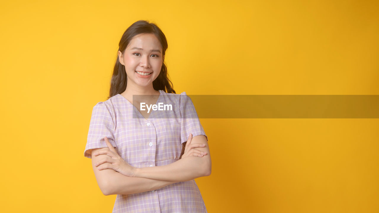 PORTRAIT OF SMILING TEENAGE GIRL AGAINST YELLOW BACKGROUND