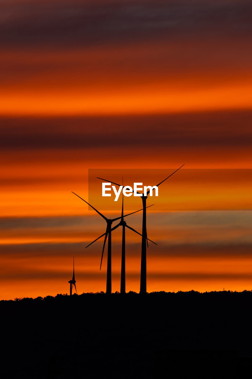 Silhouette wind turbines on field against sky during sunset