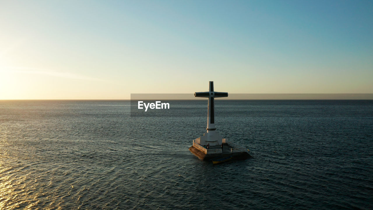 Catholic cross in sunken cemetery in the sea at sunset, aerial drone. 