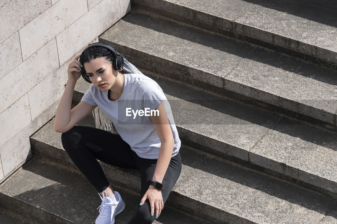 HIGH ANGLE VIEW OF YOUNG WOMAN SITTING ON STAIRCASE AGAINST WALL