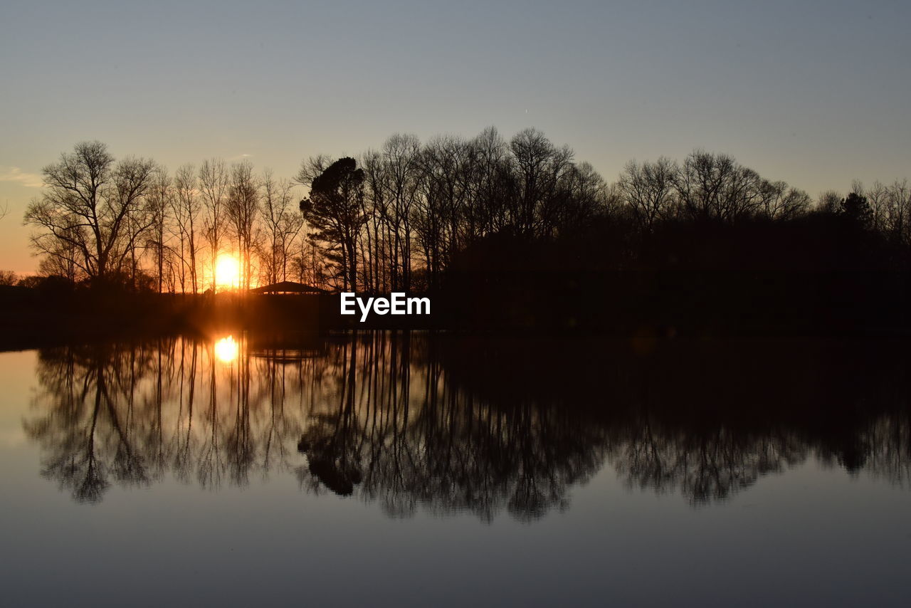 REFLECTION OF SILHOUETTE TREES IN LAKE AGAINST SKY DURING SUNSET