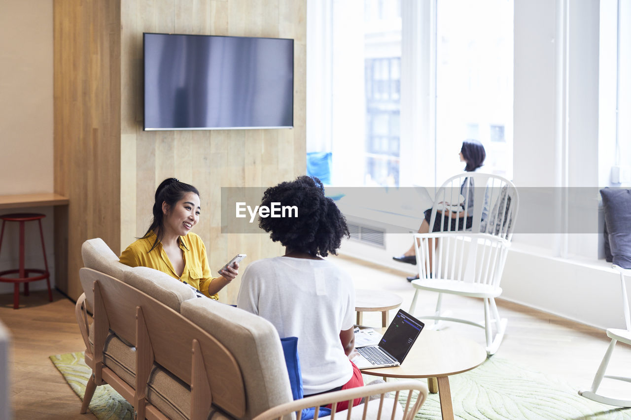 Businesswomen looking at female colleague with coworker sitting in background