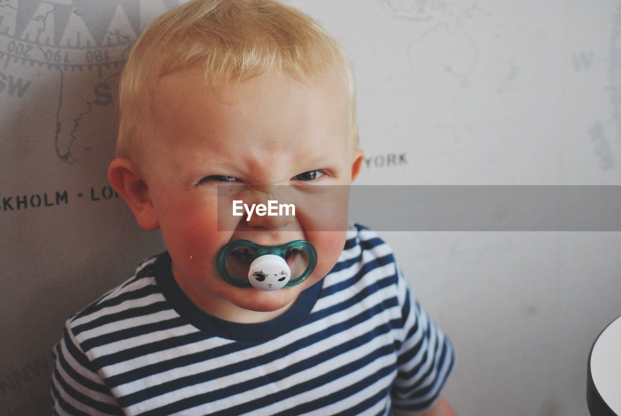 Portrait of angry baby boy sucking pacifier at home