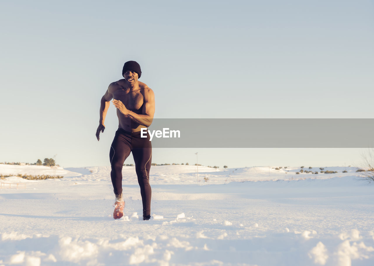 Shirtless athlete exercising while running in snow during sunset