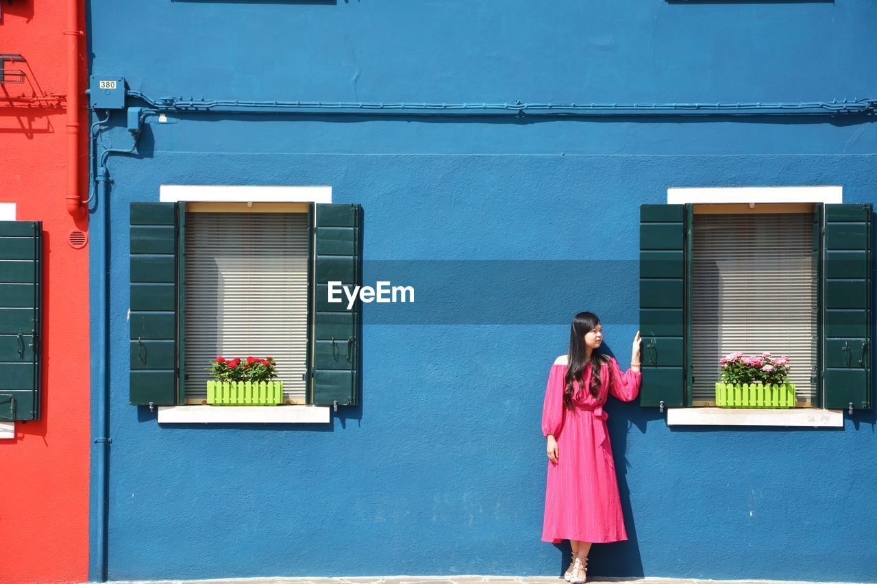 YOUNG WOMAN STANDING AGAINST WINDOW