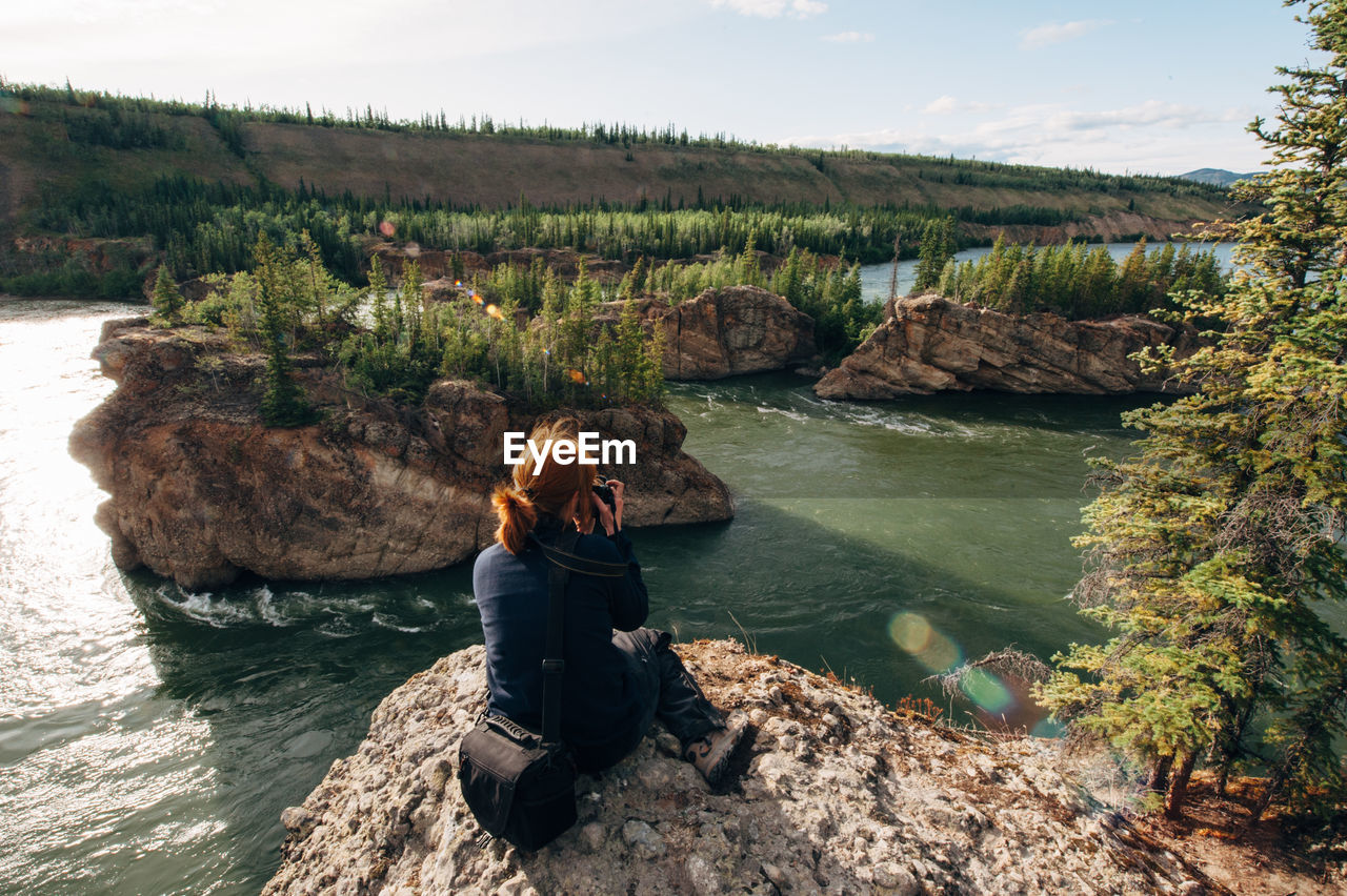 High angle view of mature woman sitting on cliff against river