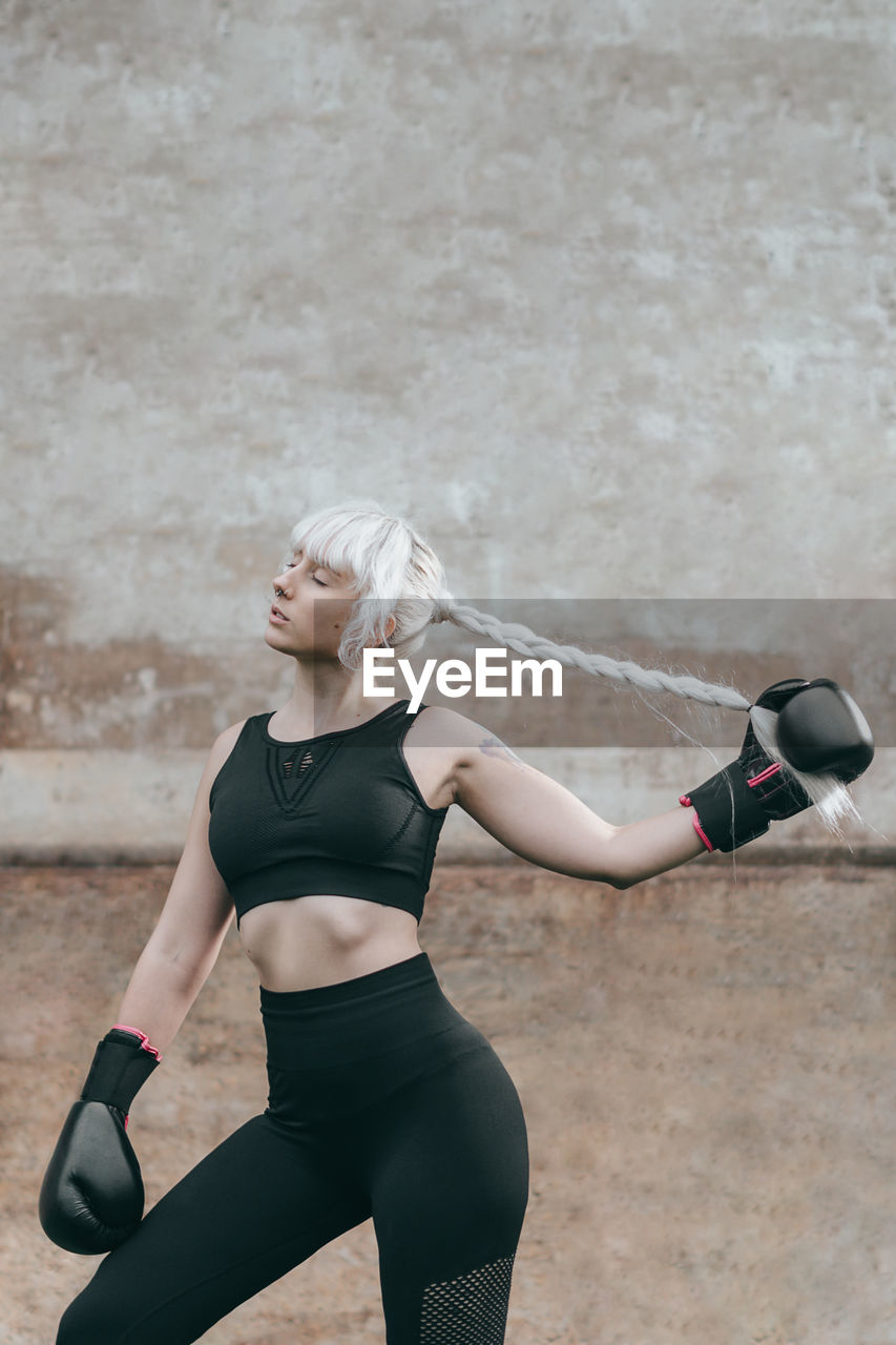 Portrait of woman with boxing gloves standing against wall