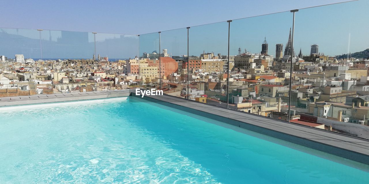 Swimming pool by buildings against clear blue sky