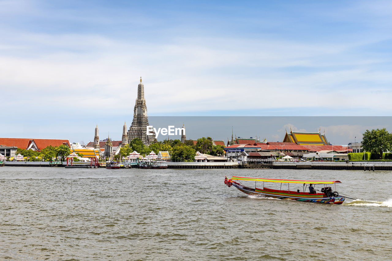 A long-tailed boat is sailing on the chao phraya river and also get to see the wat arun riverside. 