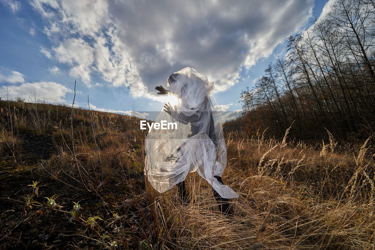 Man wrapped in plastic standing on field against sky