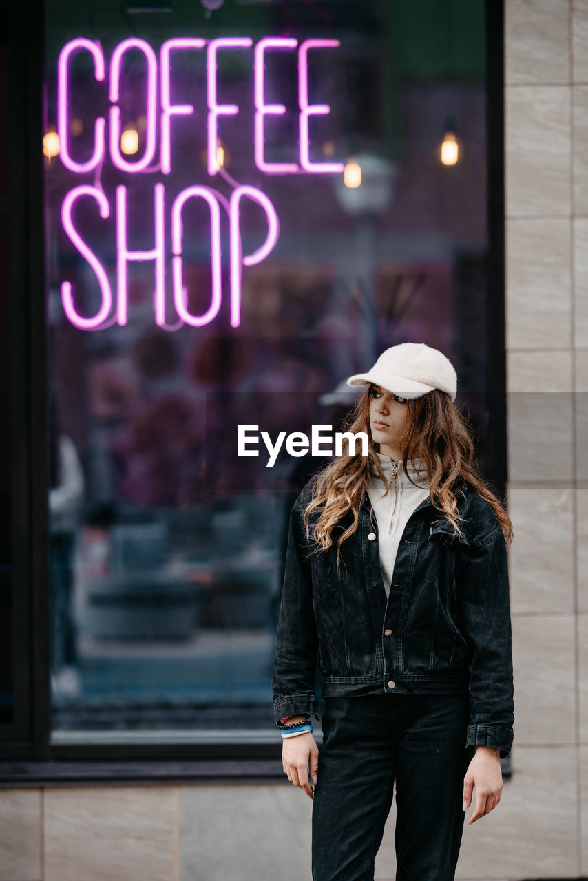 A teenage girl stands near the neon sign coffee shop. youth culture. real beautiful people. 