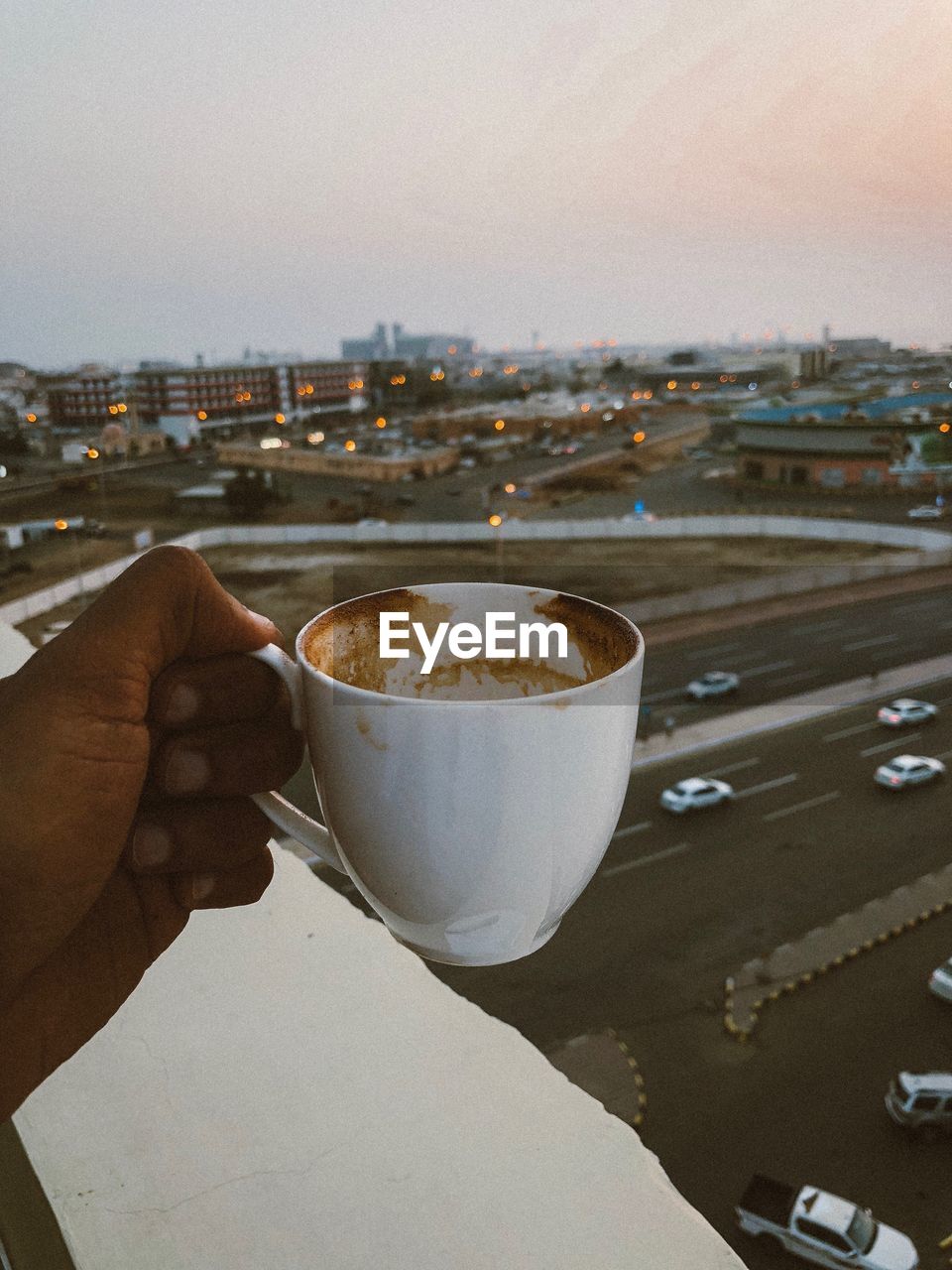 HAND HOLDING COFFEE CUP AGAINST SKY IN CITY AGAINST CLEAR BLUE BACKGROUND